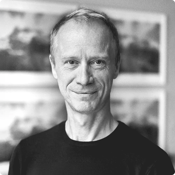Black and white portrait of Peter with short hair wearing a black shirt, smiling slightly with a blurred background.