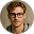 Portrait of a young man with glasses and curly hair against a mustard yellow background.