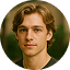 Young man with wavy light brown hair and green eyes wearing a black shirt against a blurred green background.