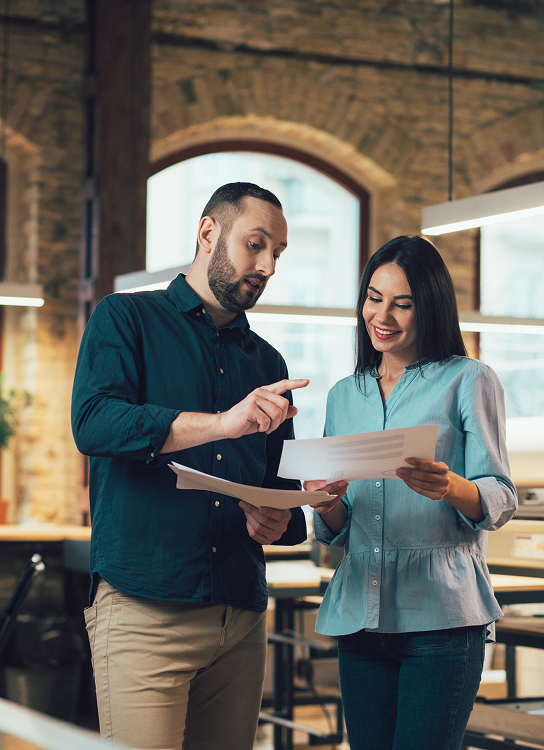 Man and woman discussing documents in a modern office with large arched windows.