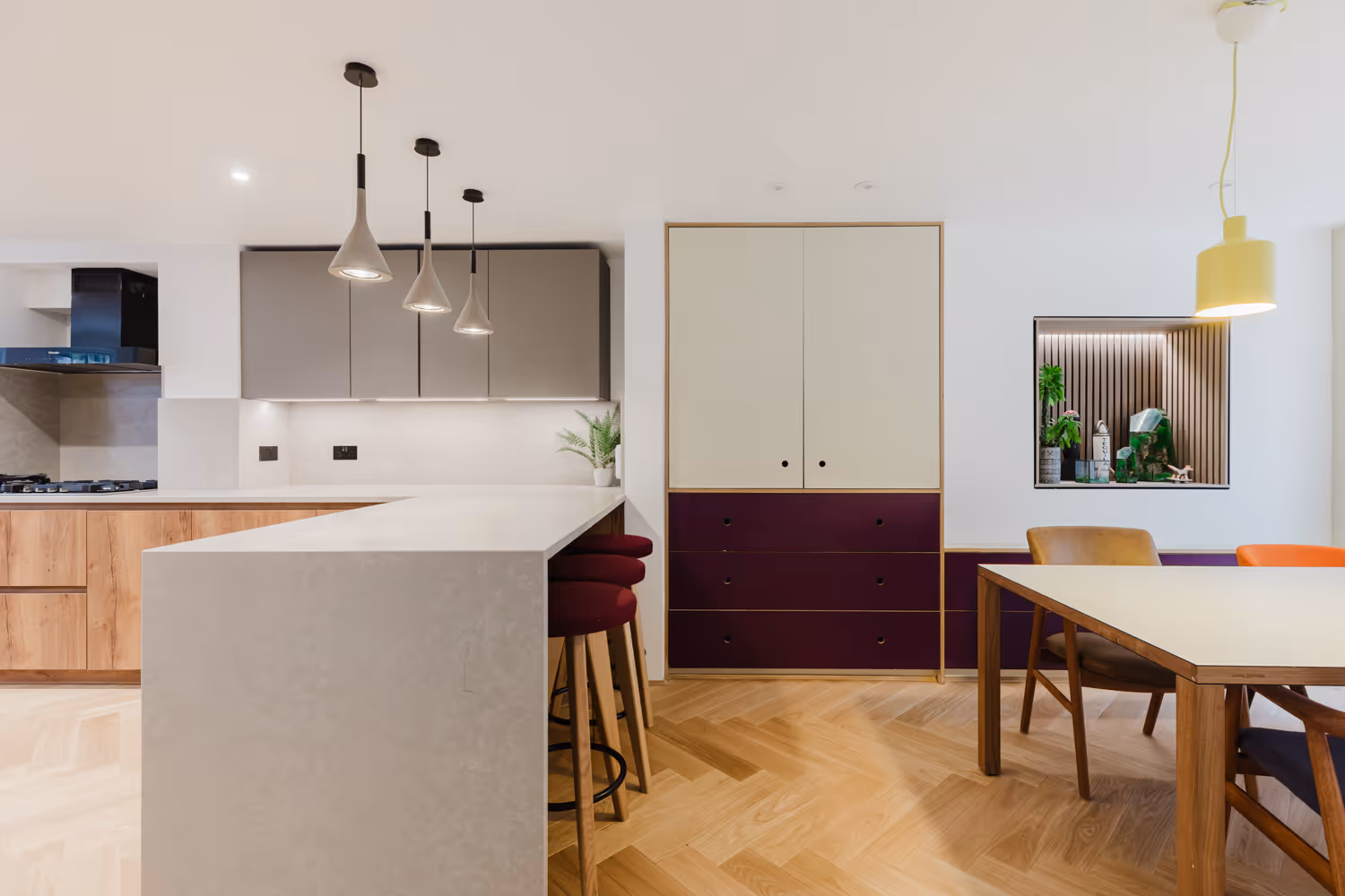 Modern kitchen and dining area with beige island, gray cabinets, purple drawers, and wooden floor.