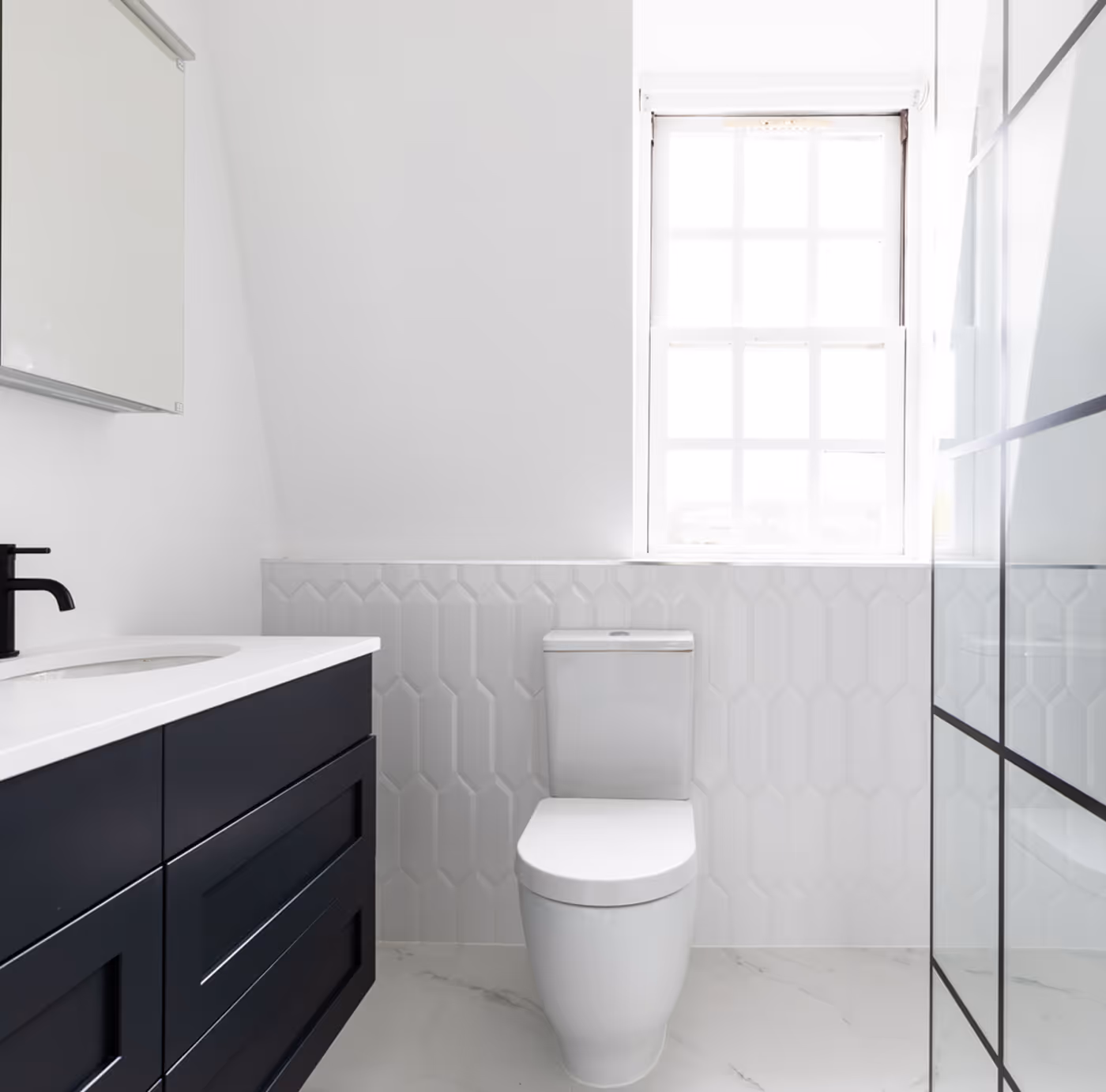 Minimalist bathroom with white toilet, black vanity with white countertop, and tiled wall under window.