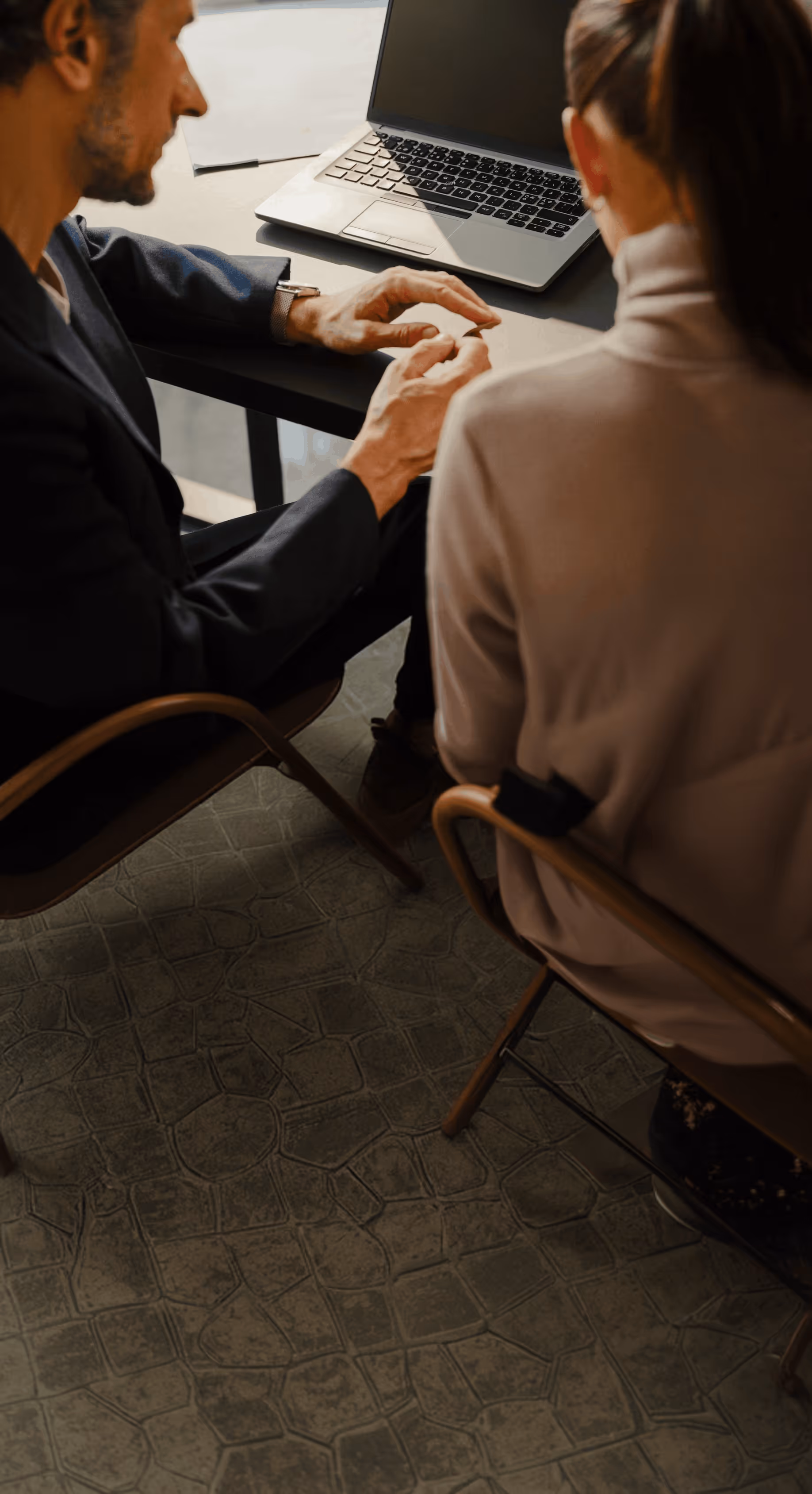 Man and woman sitting at a table with a laptop, engaged in conversation or discussion.