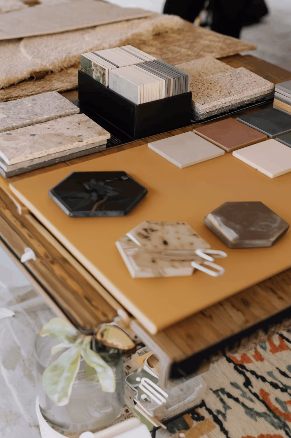 Various tile and material samples in different shapes and colors arranged on a wooden table.