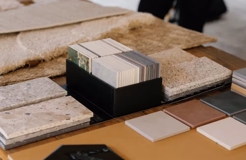 Various types of rectangular stone and tile samples arranged on a wooden table.