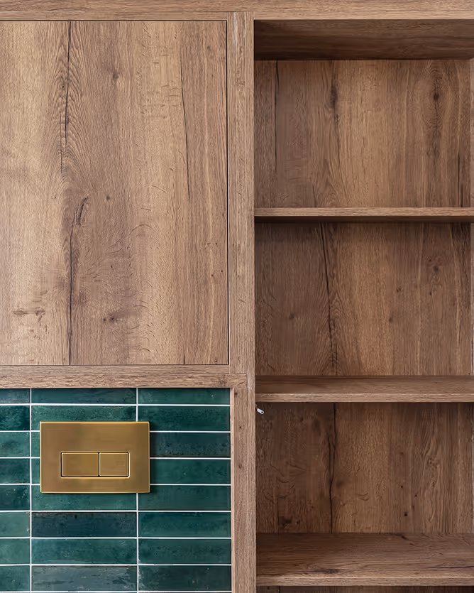 Wooden cabinet with green tiled backsplash and a brass dual flush plate in a kitchen setting.