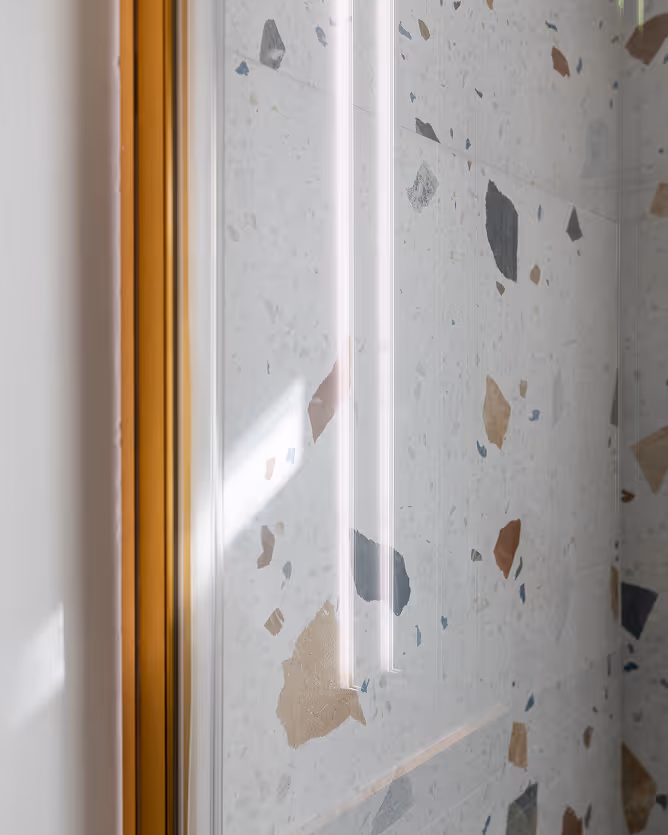 Wall with terrazzo tiles in various colors and a wooden door frame on the left side.