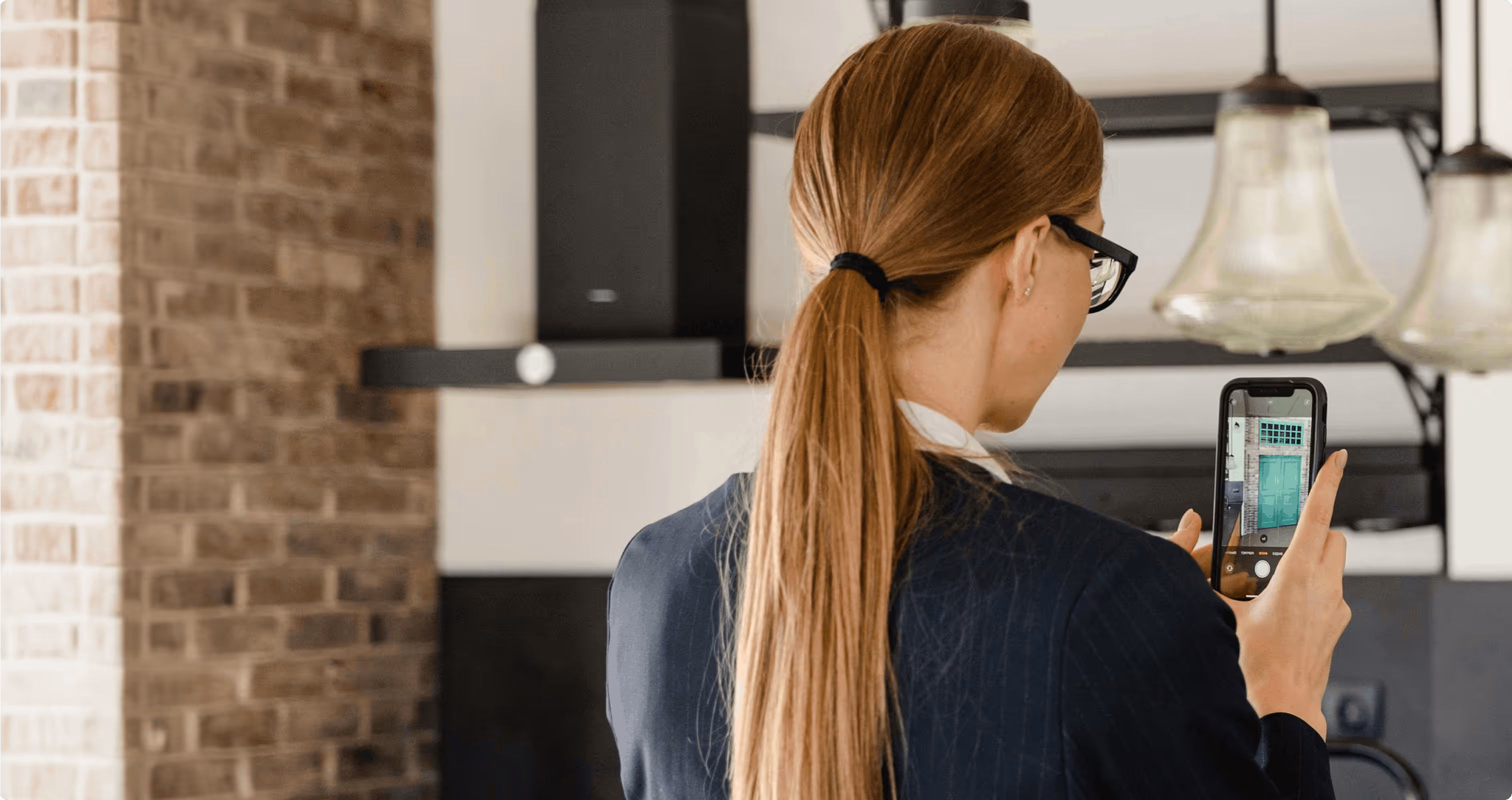 Woman with glasses and ponytail taking a photo of a green door using a smartphone indoors.