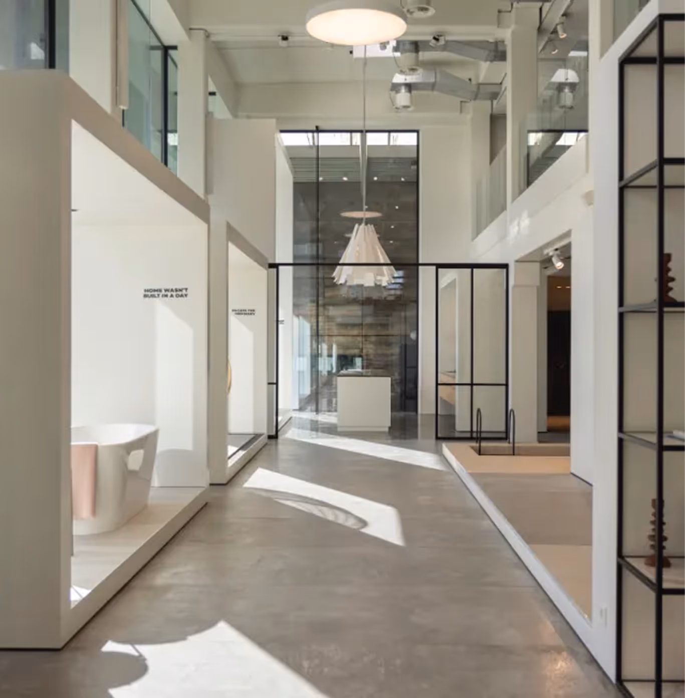 Bright modern showroom with white walls, glass partitions, minimal decor, and pendant lighting.