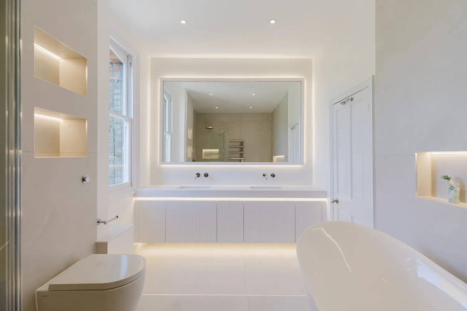 Completed Indesign bathroom with double vanity, freestanding bath, wall-hung WC and illuminated storage
