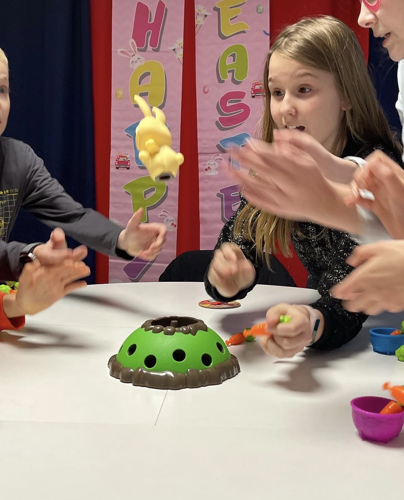 Children playing a game where a yellow bunny toy is flying above a green dome with holes.
