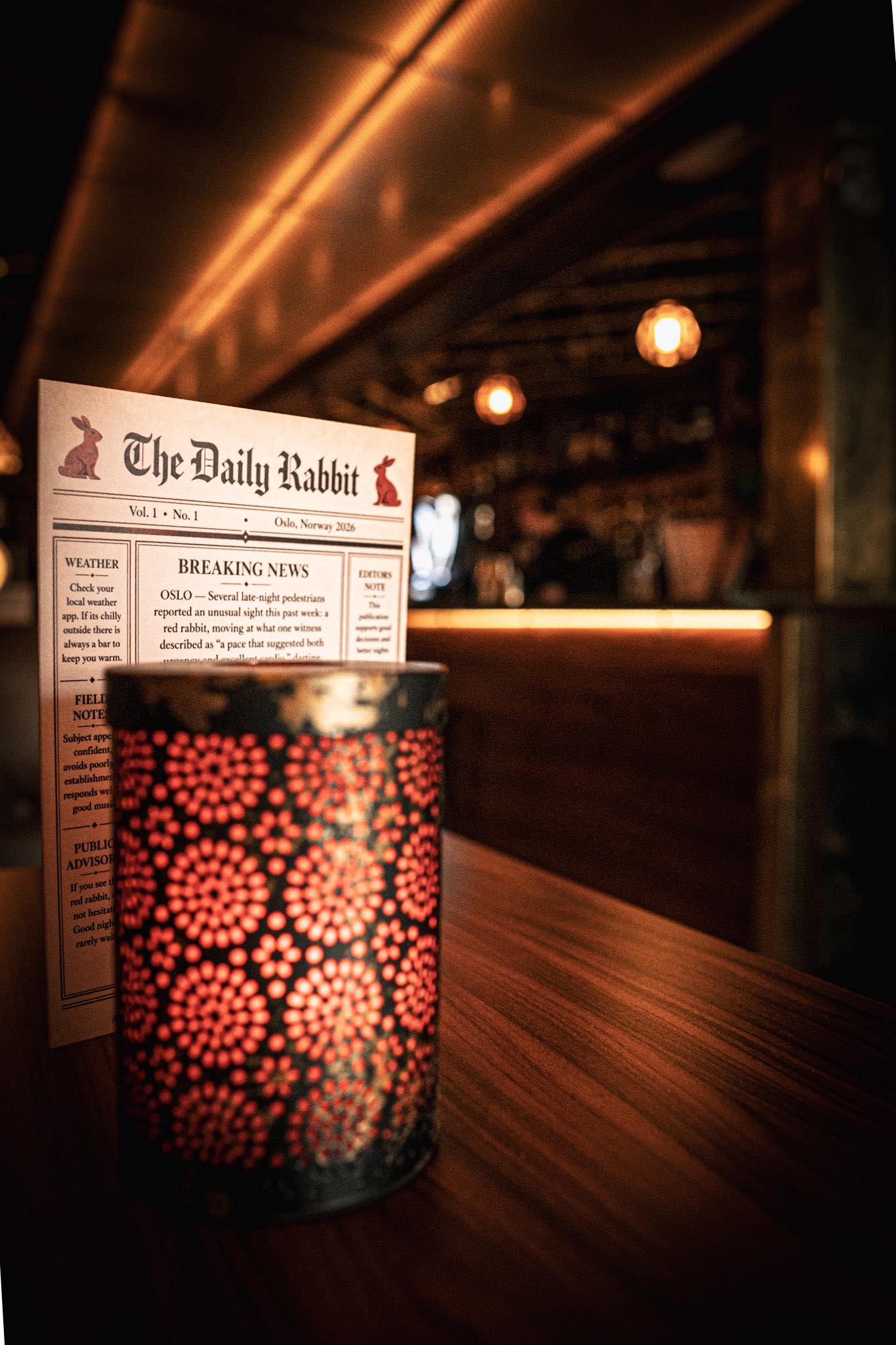 The Daily Rabbit pub newspaper on a table at Red Rabbit Oslo, warm amber lights and dark wood pub atmosphere