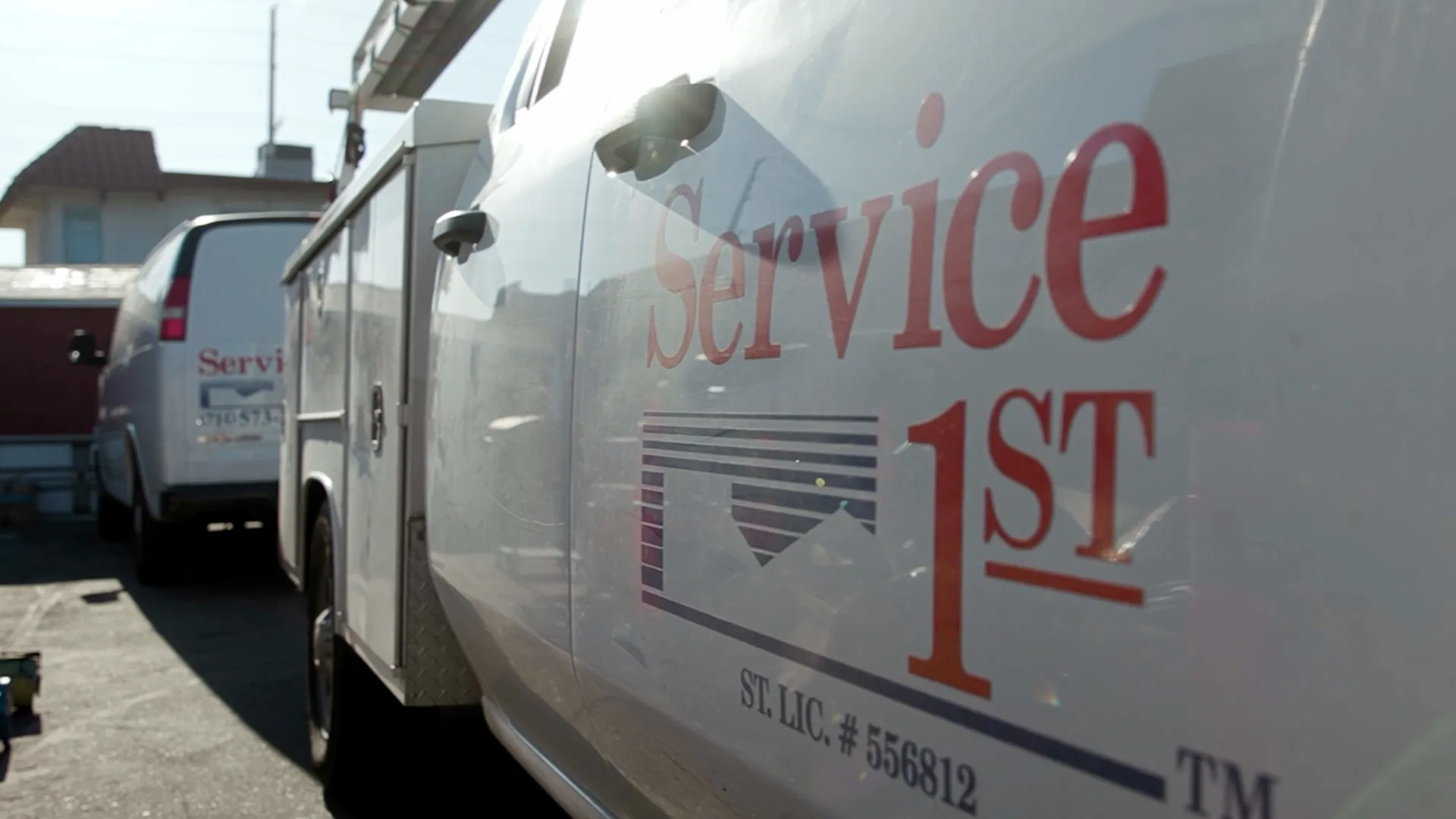 Close-up of a white service truck with the red and blue Service 1st logo on the side, parked next to another service vehicle.