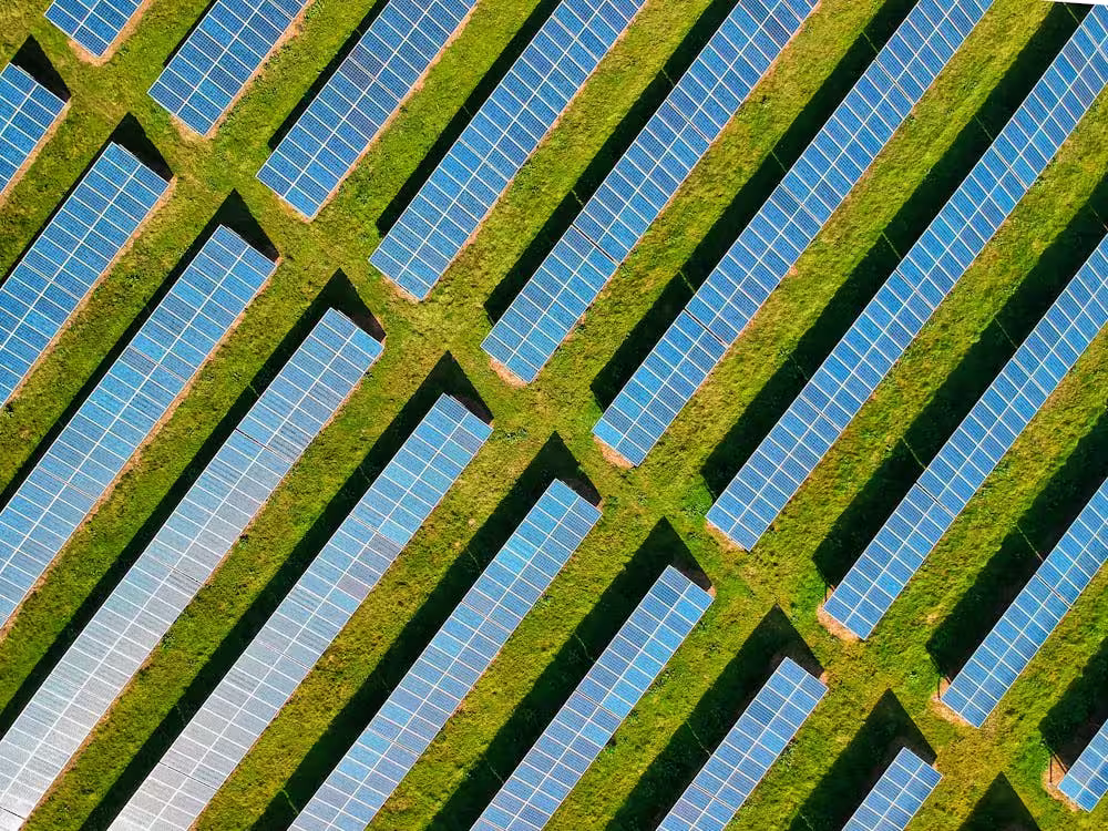 Aerial view of a solar farm with numerous rows of blue solar panels installed on green grass.