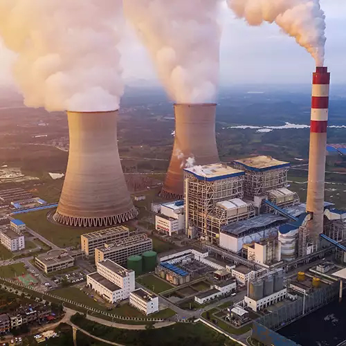 Aerial view of a coal power plant with large cooling towers and a smokestack emitting dense steam or smoke.