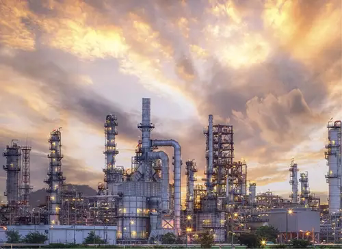 Large petrochemical refinery with numerous towers and pipes under a dramatic cloudy sunset sky.