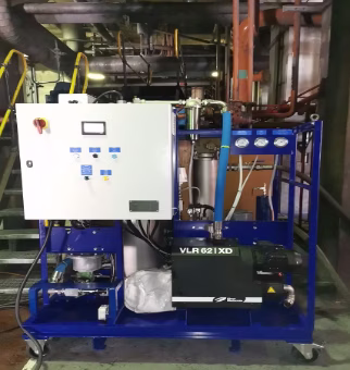 Industrial mechanical equipment unit with control panel, gauges, pipes, and a black component labeled VLR 62 XD on a blue metal frame with yellow handrails and stairway in background.