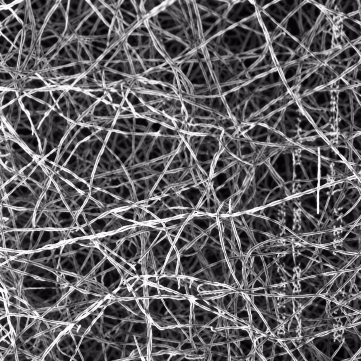 Close-up of tangled metallic fibers forming a dense, chaotic mesh pattern in grayscale.