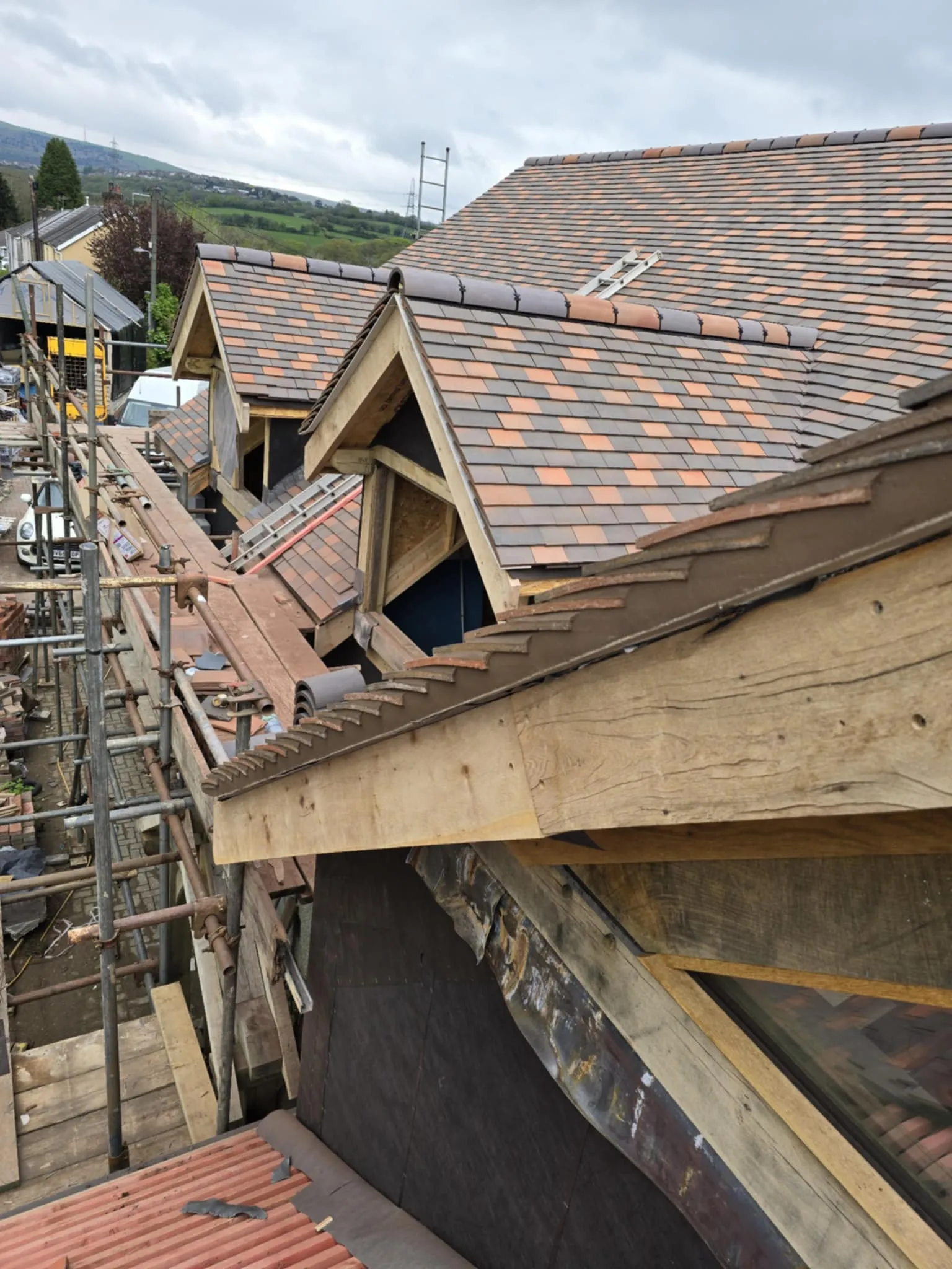 Construction view of a row of houses with newly tiled pitched roofs and wooden scaffolding along the side.