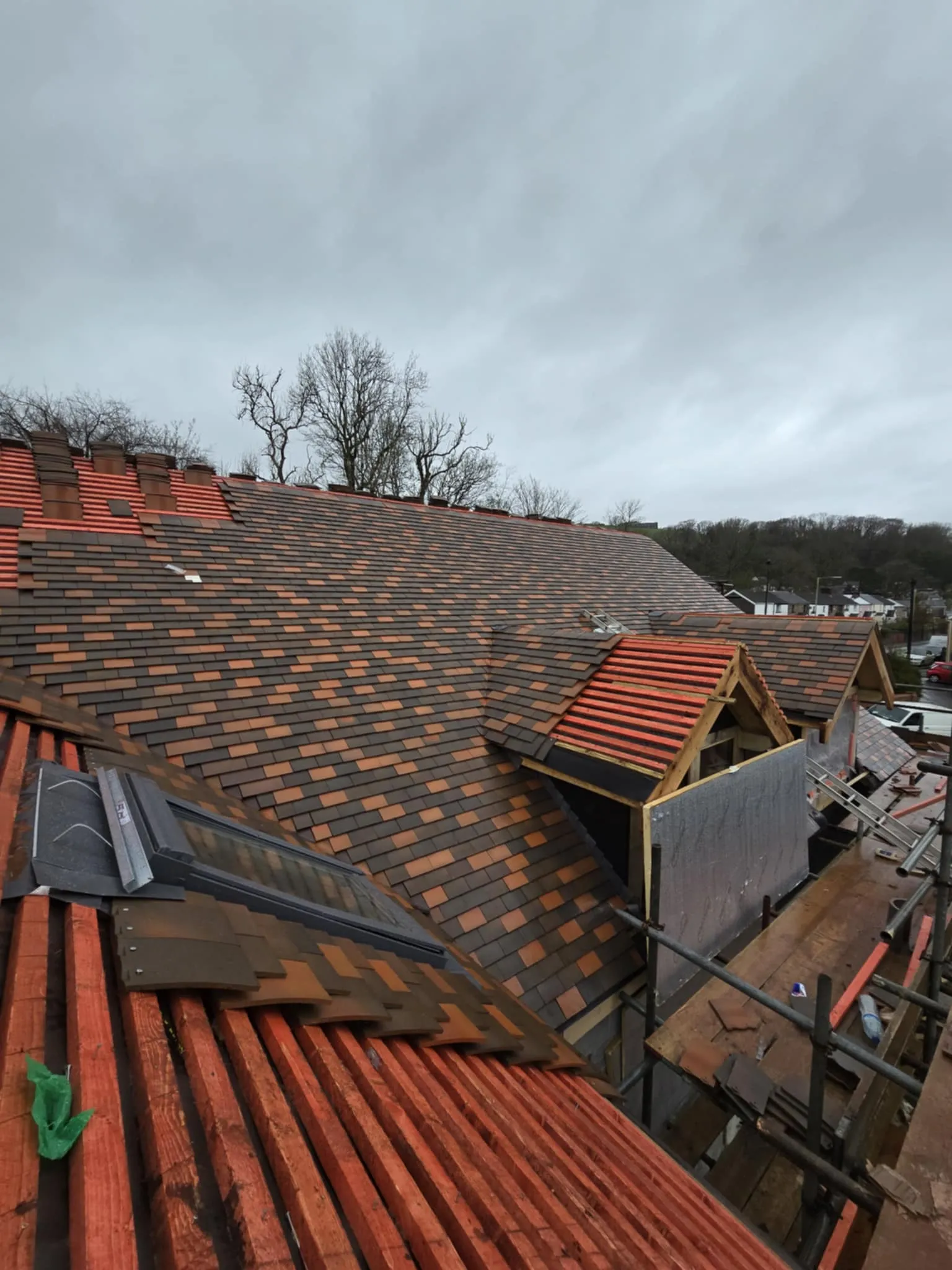 Partially tiled roof of a building under construction with scaffolding and overcast sky.