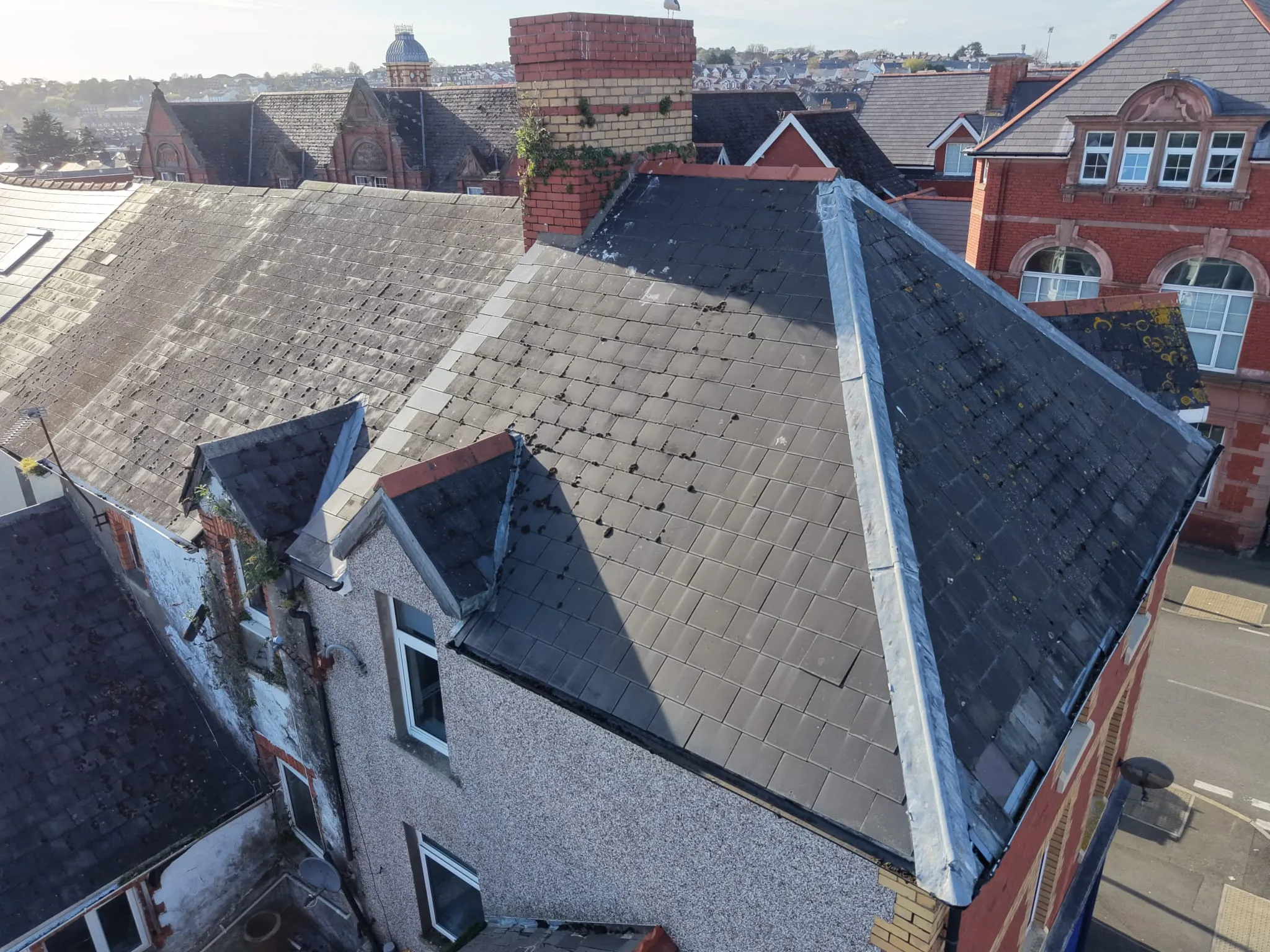 Aerial view of old residential buildings with slate roofs, brick chimneys, and some ivy growing on the walls under clear sky.