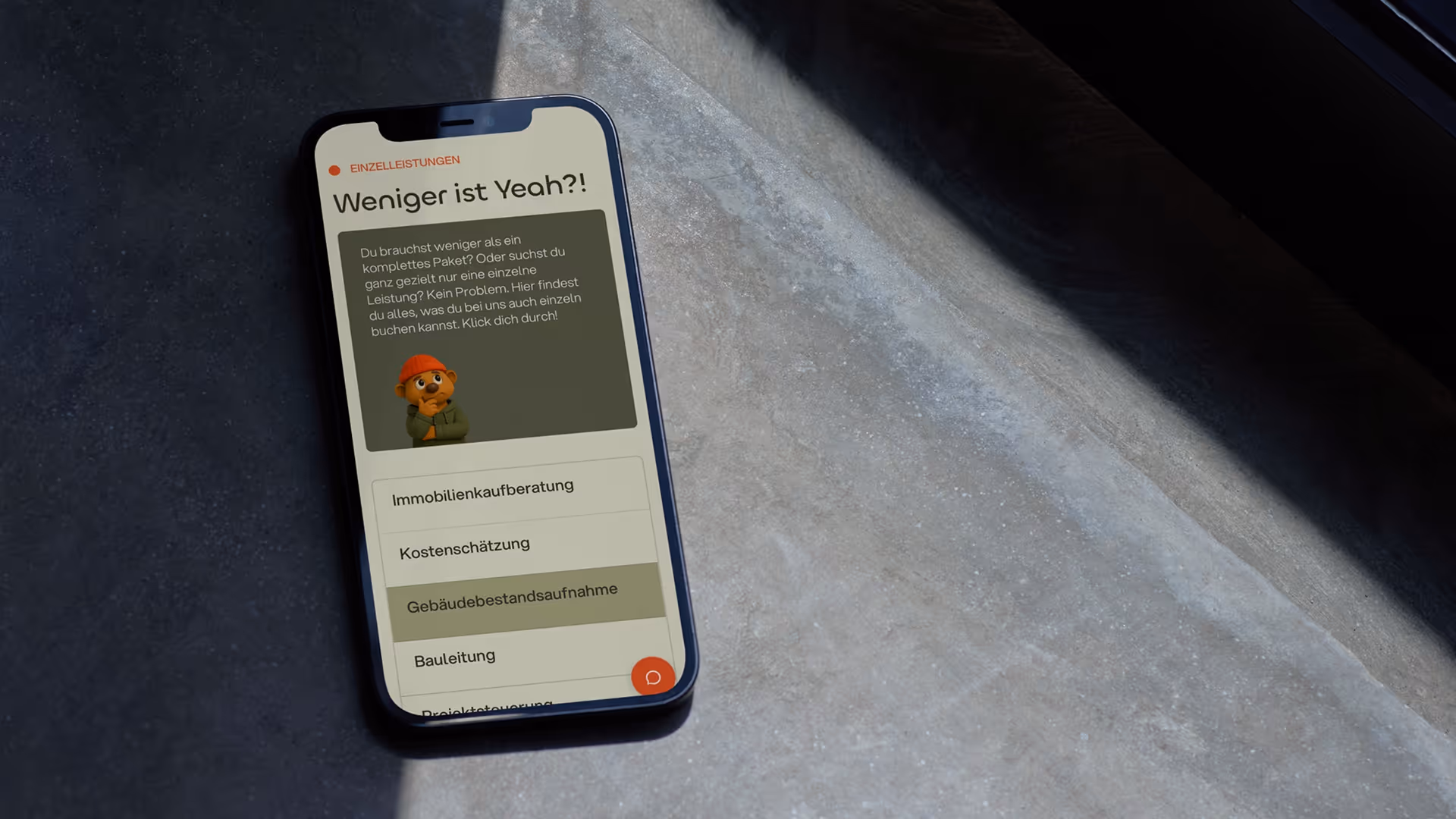 Smartphone zeigt eine Webseite mit dem Titel 'Weniger ist Yeah?!' und einer Liste von Einzelleistungen wie Immobilienkaufberatung und Kostenschätzung.