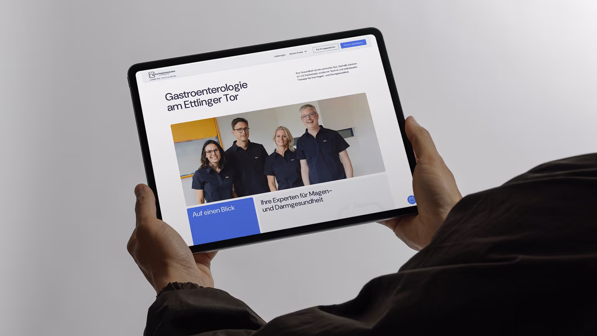Person hält ein Tablet, das die Webseite einer gastroenterologischen Praxis mit vier Teammitgliedern zeigt.