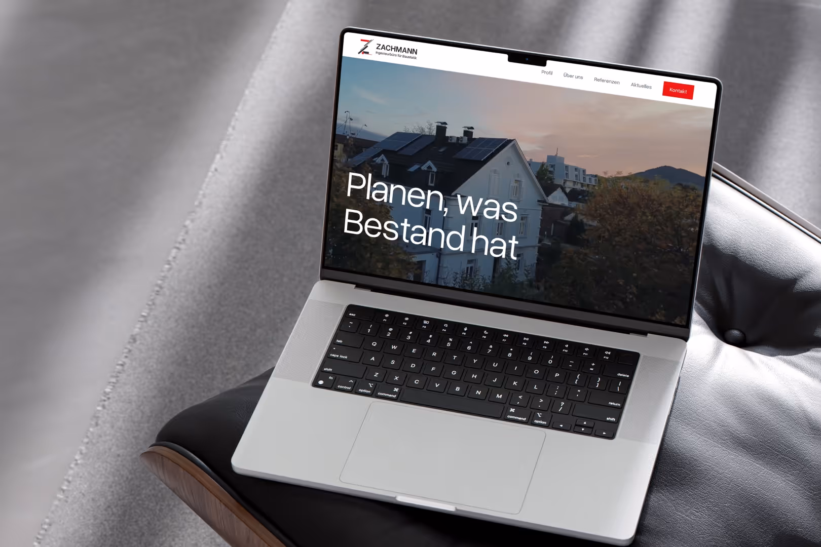 Offener Laptop auf einem Stuhl zeigt eine Webseite mit deutschem Text und einem Haus mit Solarpanelen im Hintergrund.