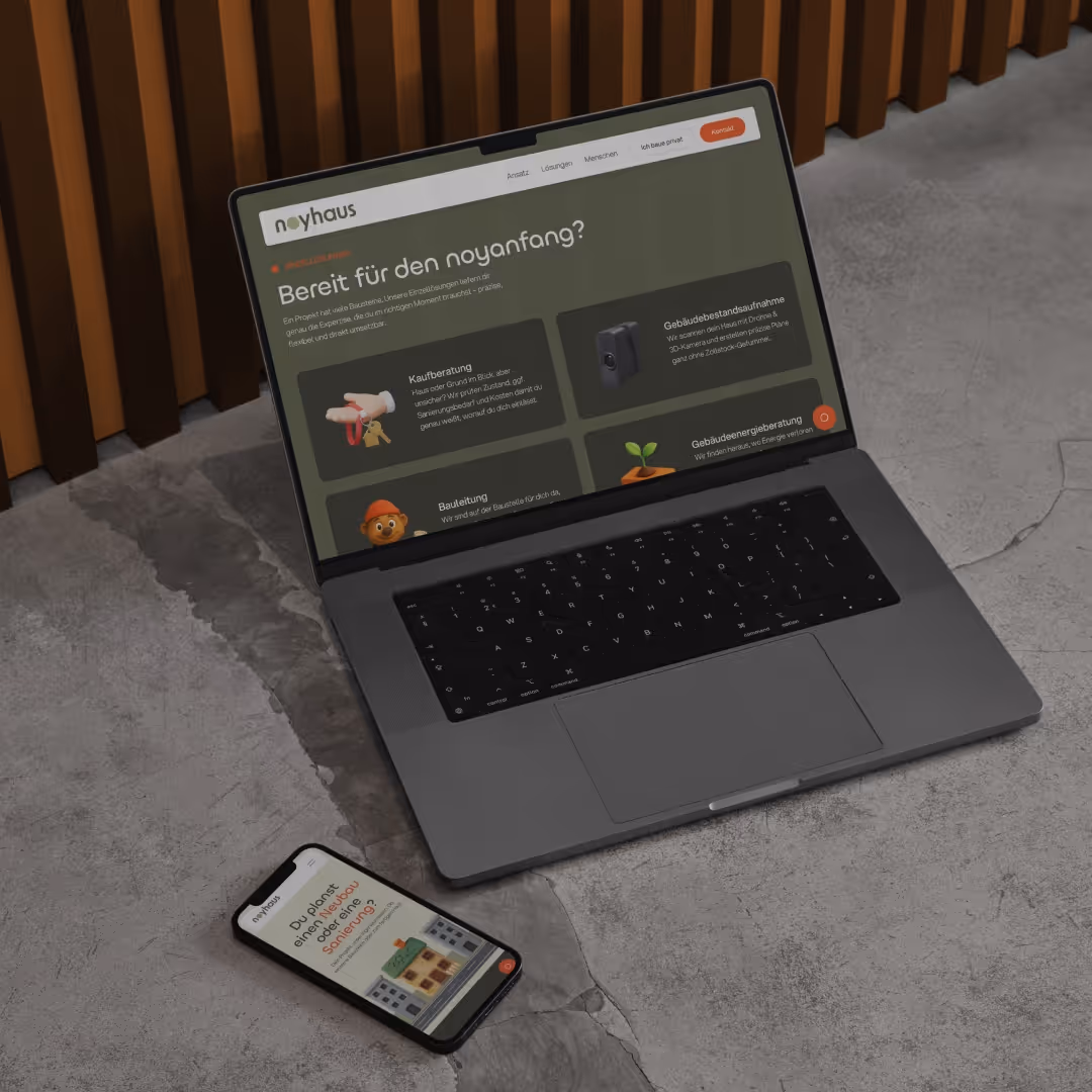 Laptop mit geöffneter Website von noyhaus mit der Überschrift ‚Bereit für den neuanfang?‘ und Smartphone daneben auf grauem Betonboden.