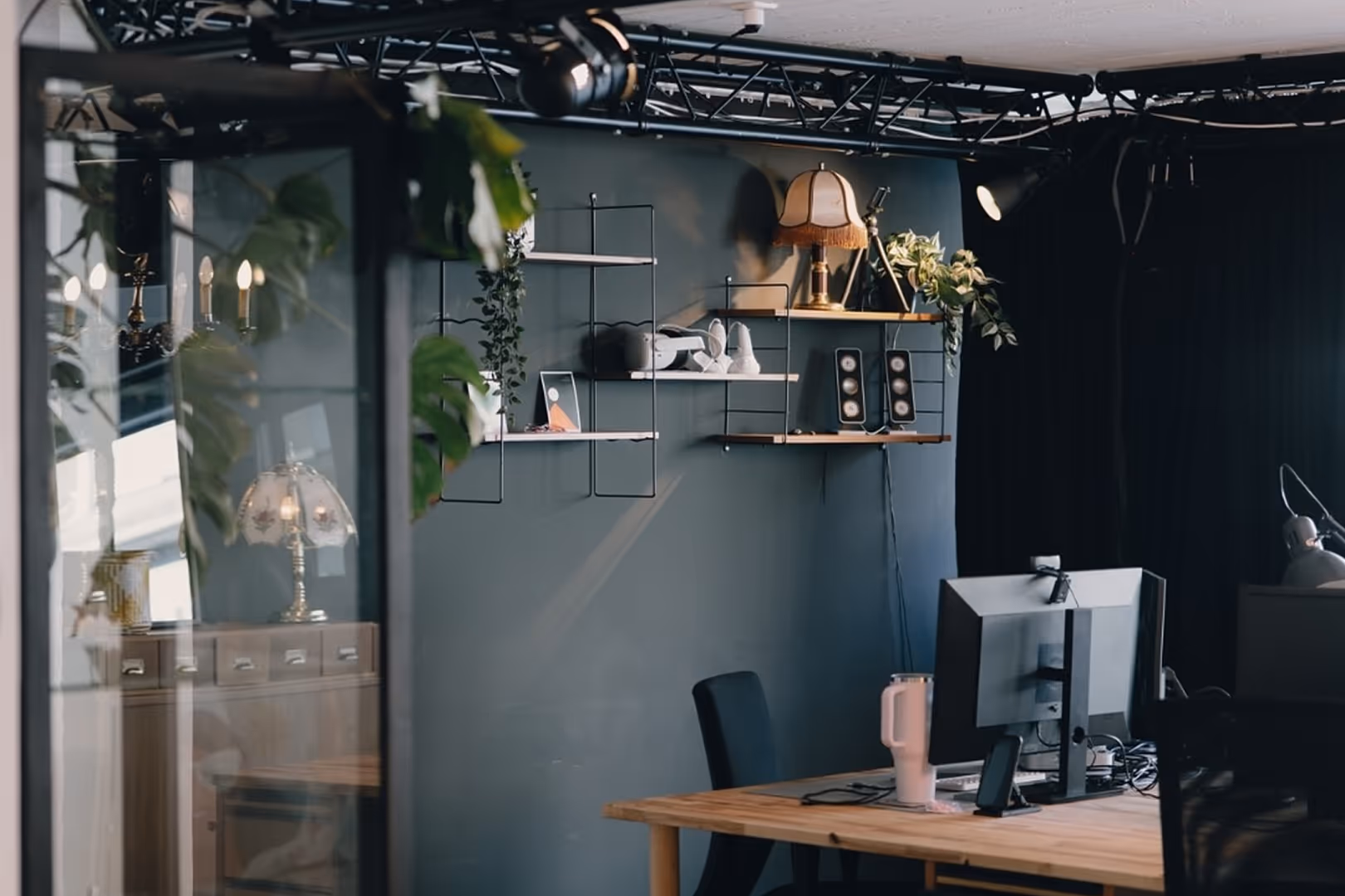 Modernes Büro mit Holzschreibtisch, zwei Monitoren, schwarzem Stuhl und Wandregalen mit Dekoration und Pflanzen.