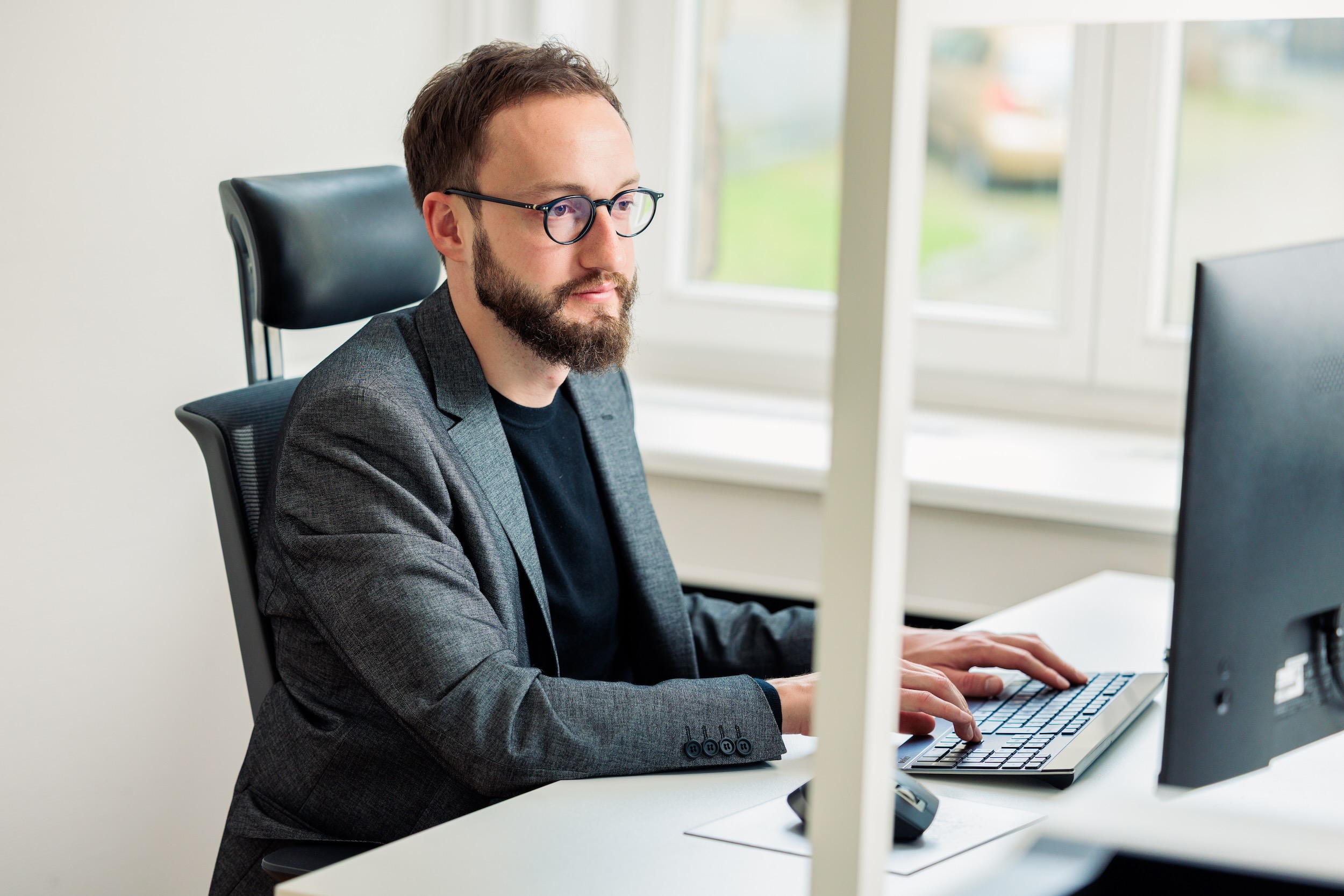 Ein Mann mit Brille sitzt an einem Schreibtisch und schaut auf einen Bildschirm.