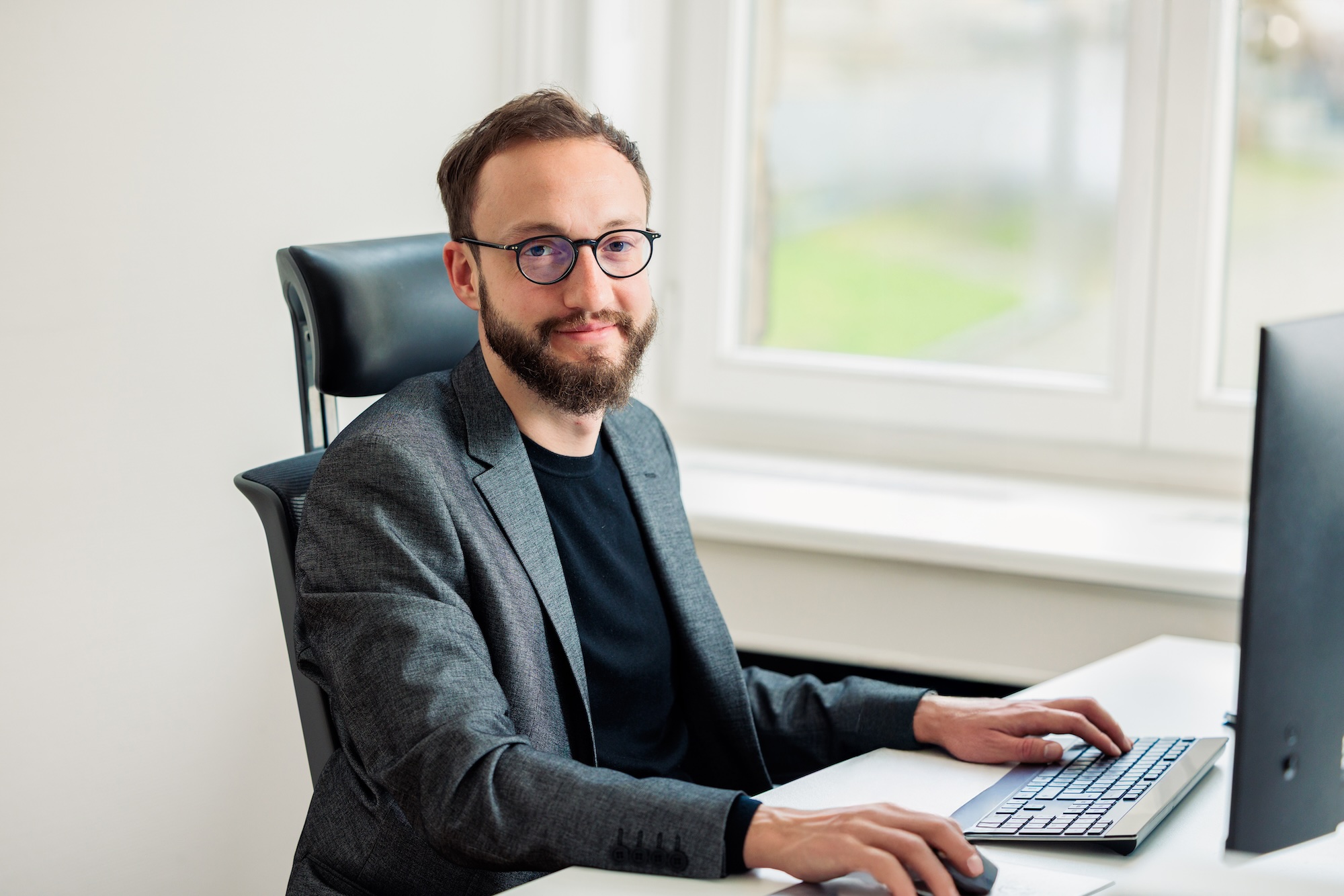 Ein Mann mit Brille sitzt an einem Schreibtisch und lächelt in die Kamera