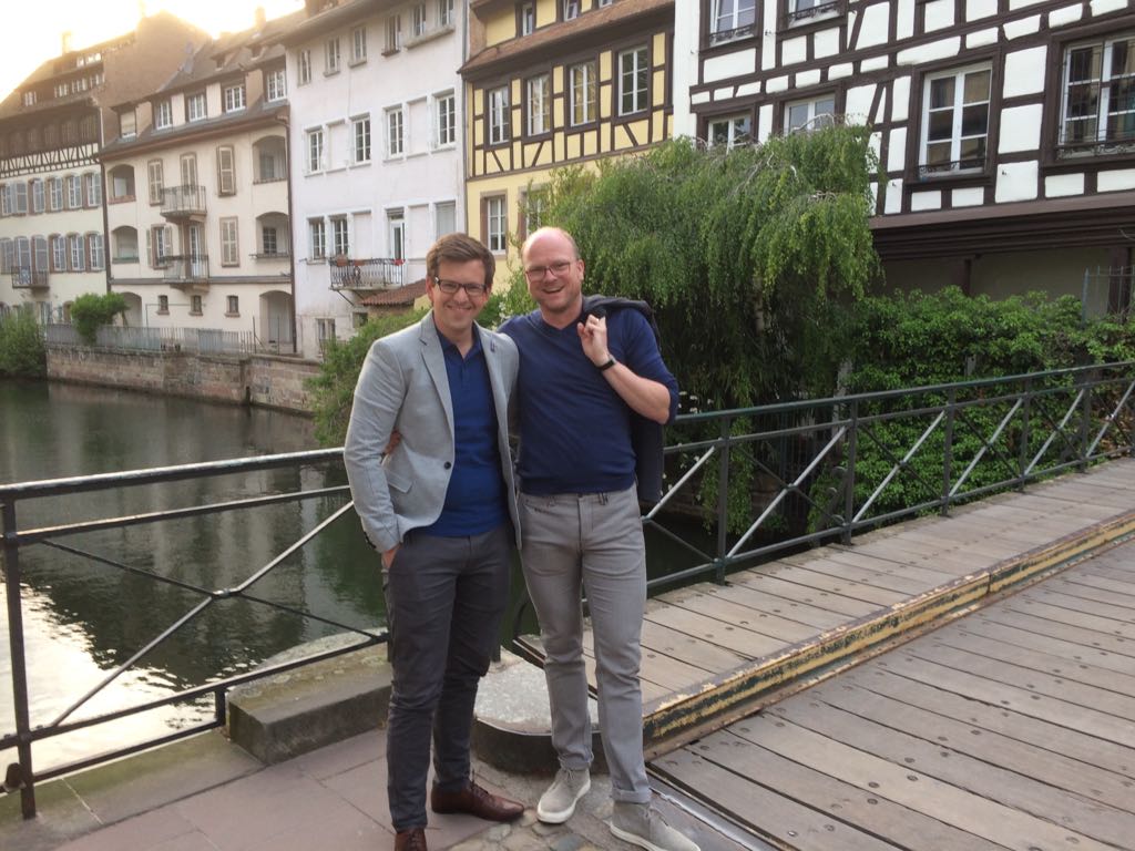 Zwei Männer stehen Arm in Arm auf einer Brücke.