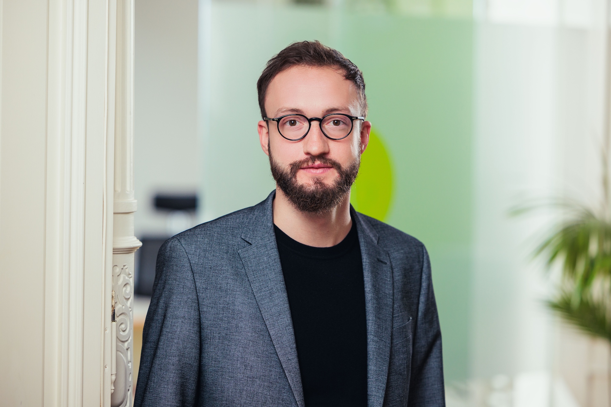 Porträt eines brünetten Mann mit Brille und grauem Sakko.
