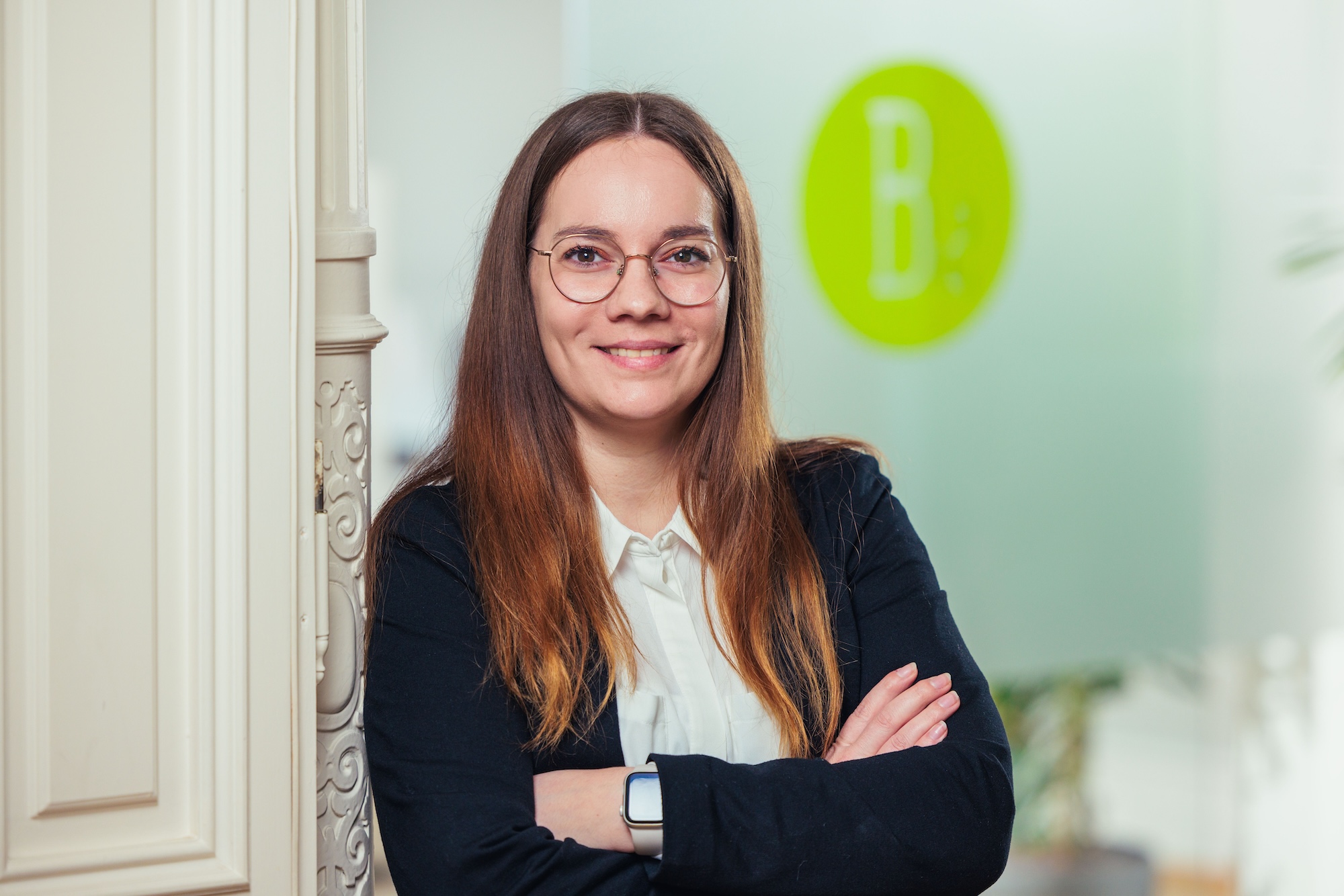 Porträt einer Frau mit hellbraunen Haaren, Brille und schwarzem Blazer.