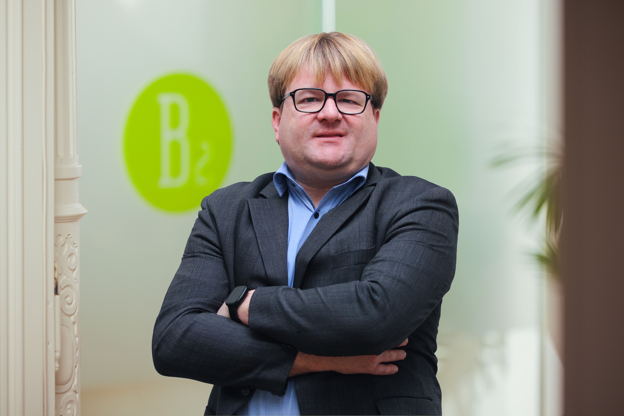 Porträtfoto eines blonden Mannes mit Brille und dunklem Sakko.