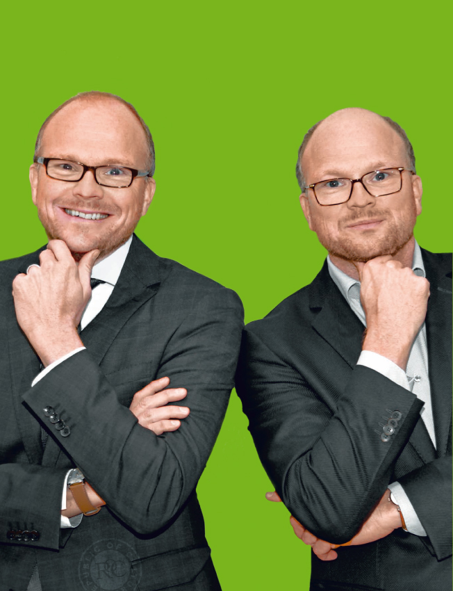 Die zwei Geschäftsführer schauen in die Kamera und stehen vor einem grünen Hintergrund.