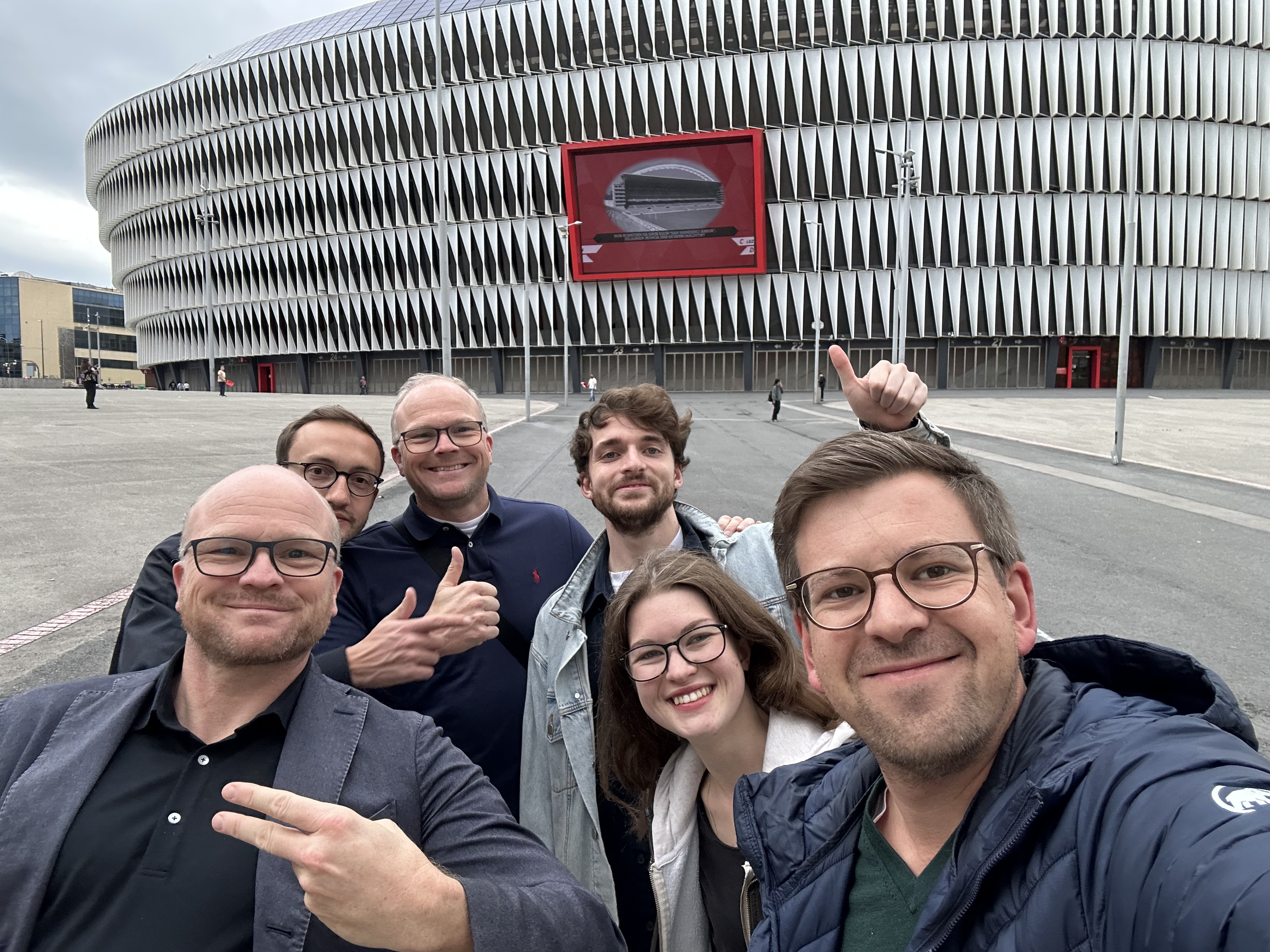 Gruppenselfie verschiedener Mitarbeiter der Kanzlei vor einem Stadion.