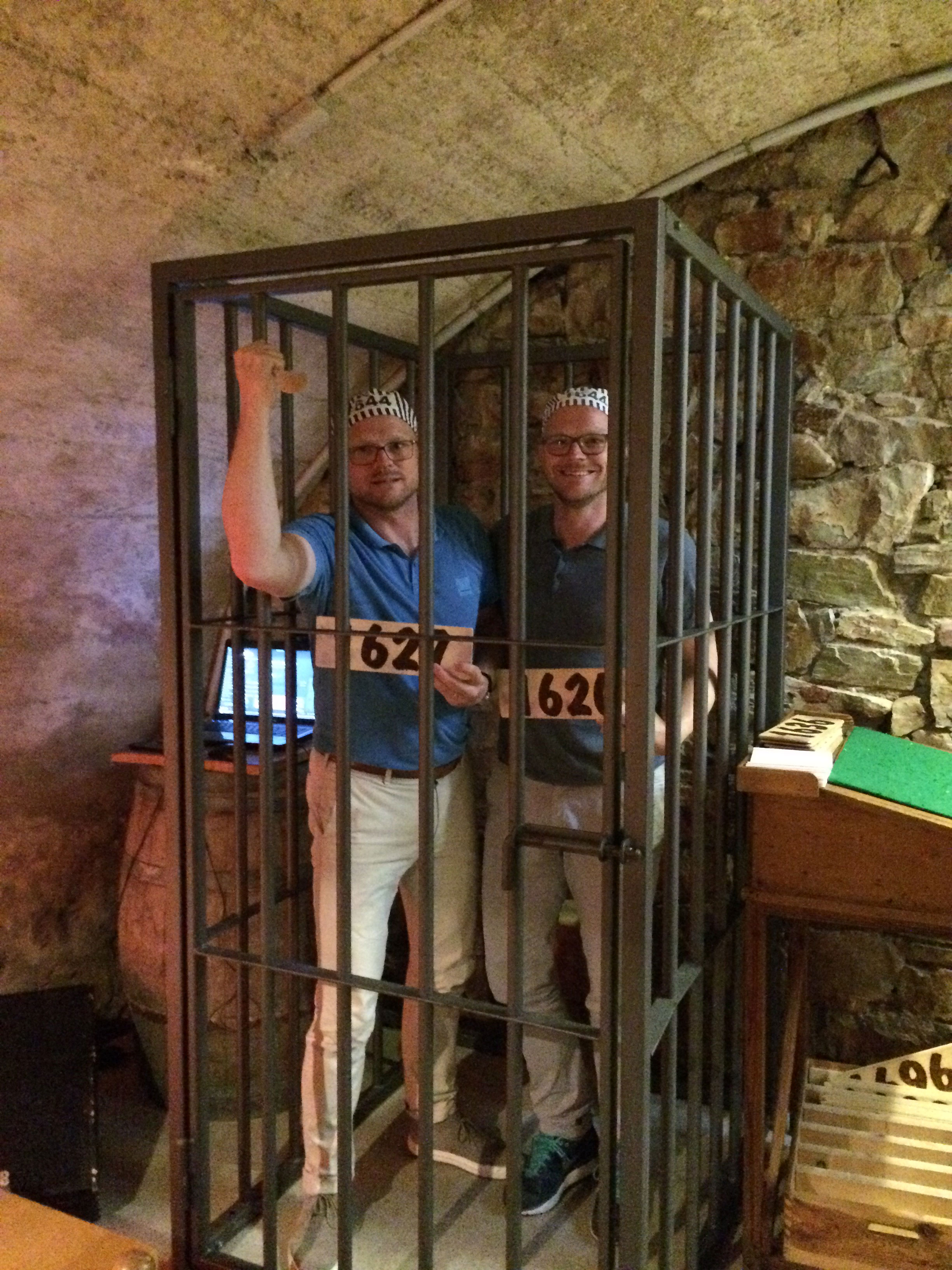 Michael und Stefan Becker bei einem Teamevent in einem historischen Käfig. Sie halten lächelt Gefangenennummern hoch.
