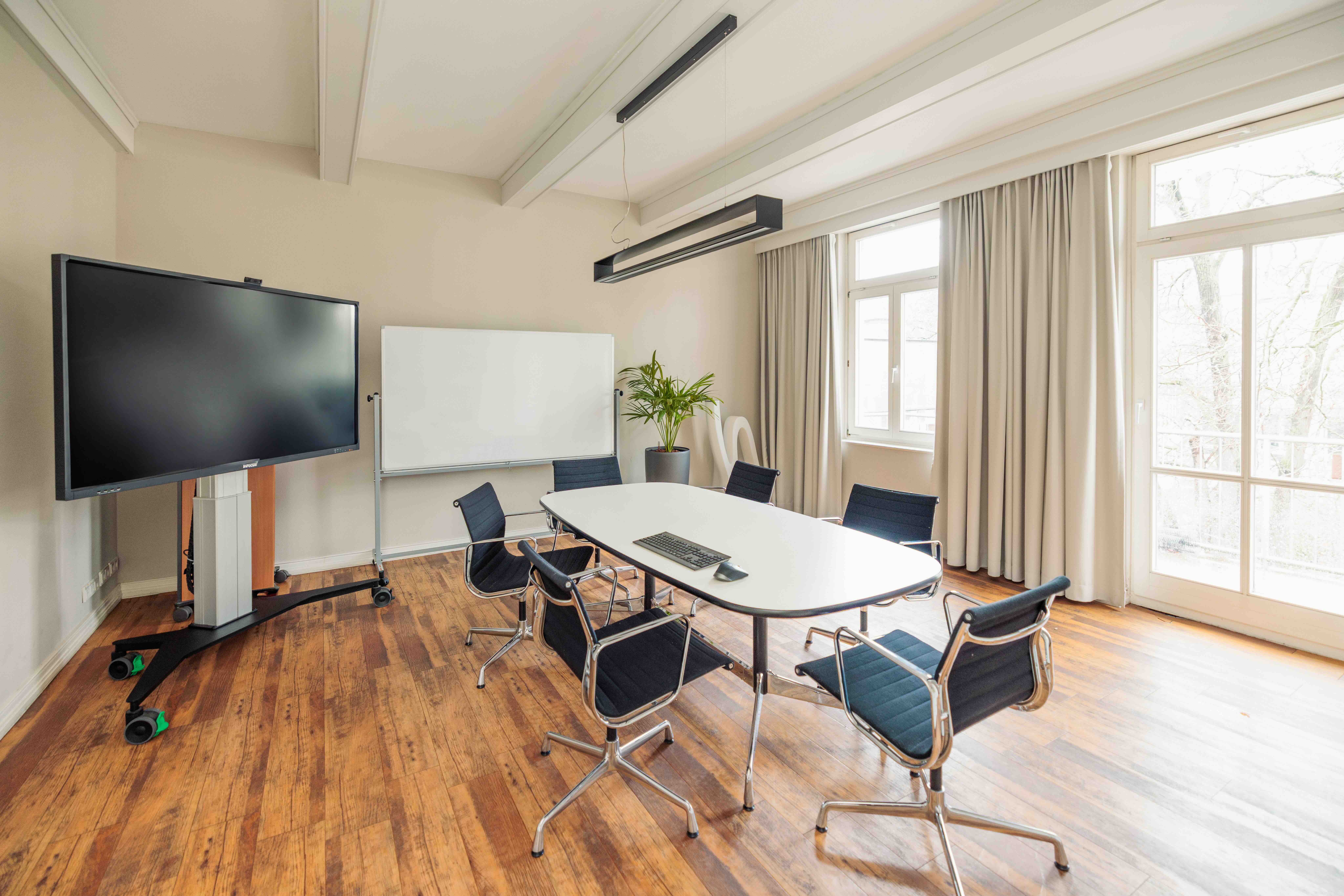 Helles Meetingbüro der Kanzlei mit einem großen ovalen Tisch, moderner großem Bildschirm und Whiteboard.