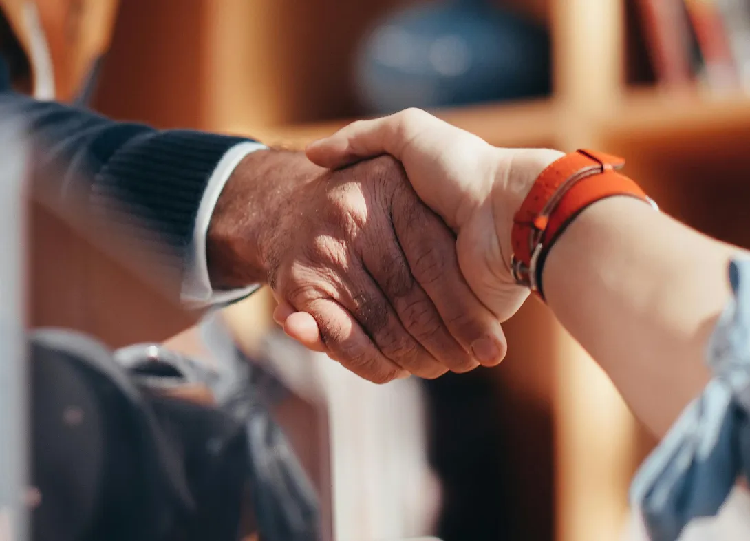 Close-up of two people shaking hands, one wearing a blue sweater and the other an orange watch.