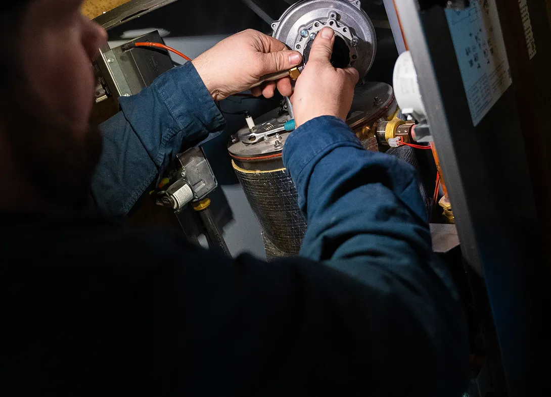 Technician adjusting components inside a heating furnace unit.
