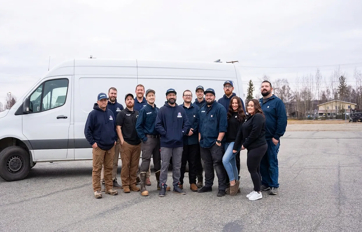 Group of twelve people, mostly men wearing work clothes, standing in front of a white van in a parking lot.