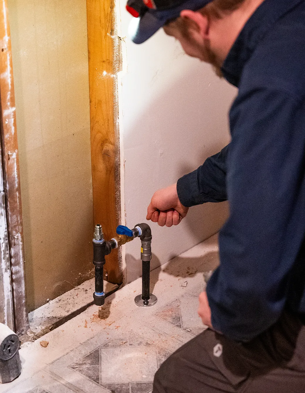 A person inspecting a newly installed plumbing pipe with a blue valve in a room with exposed wall studs.