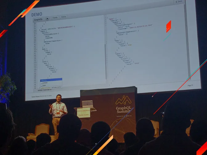 A presenter at GraphQL Summit showing a live GraphiQL code demo on a large projection screen