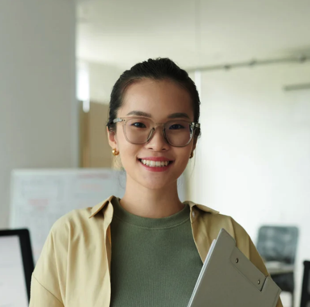 Smiling woman wearing glasses holding a clipboard in an office setting. Client picture. 