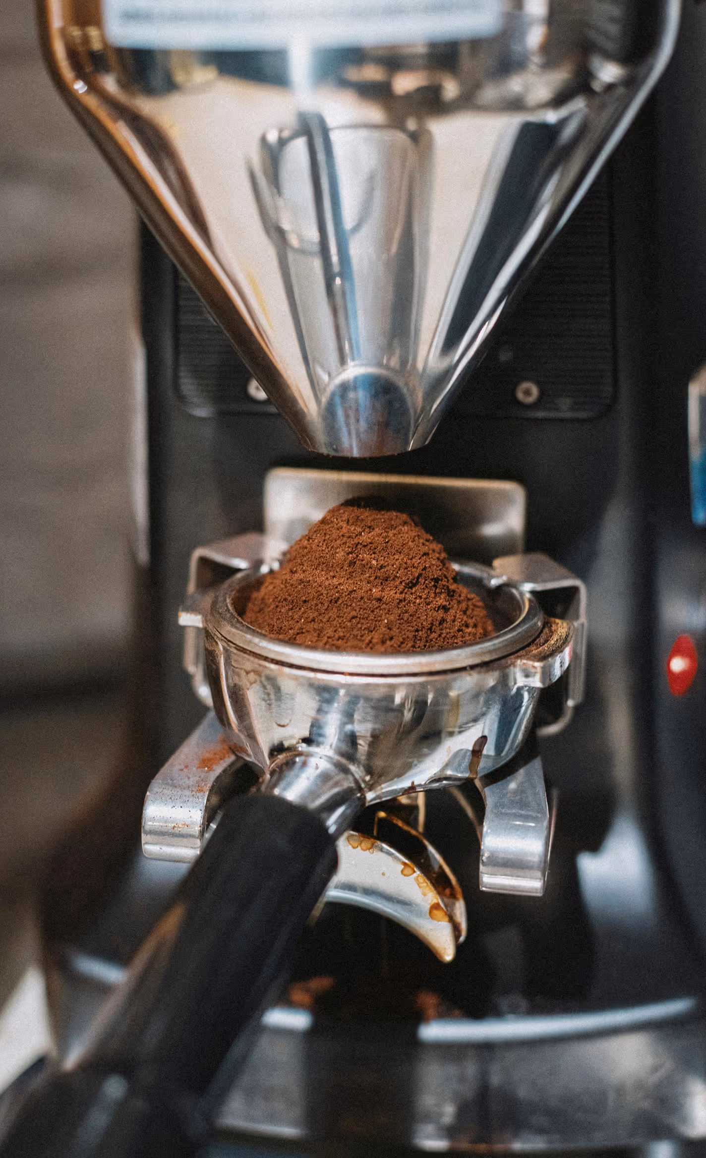 A portafilter is placed in an espresso grinder, filled with ground coffee.