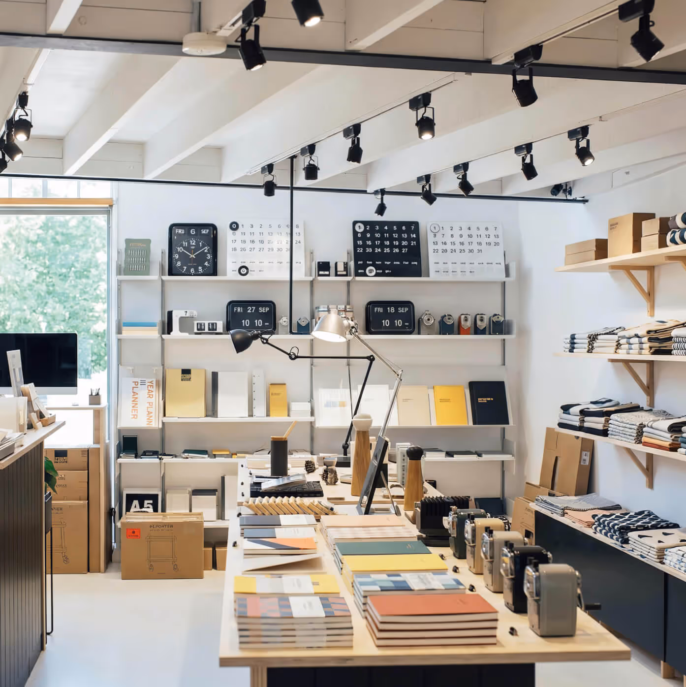 Bright airy Ajenda stationery store interior with white shelves and wooden tables