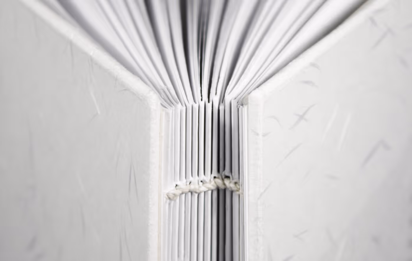 Close-up of coptic stitch binding with exposed spine and linen thread on handmade cookbook pages