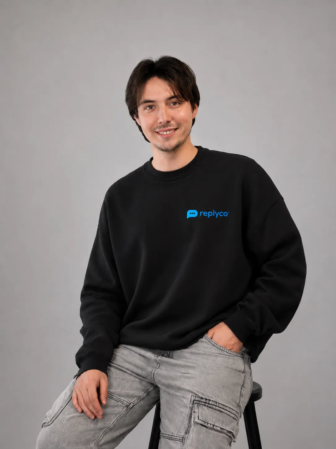 Junger Mann mit mittellangen dunklen Haaren trägt einen roten Hoodie vor grauem Hintergrund.